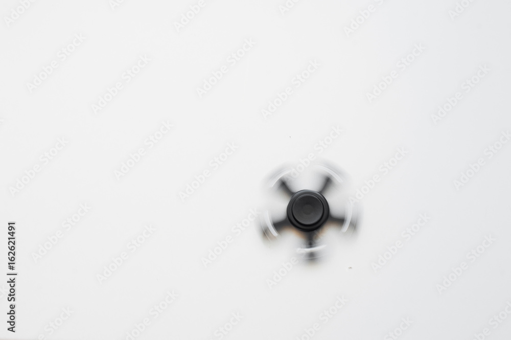 Black spinner on a white background. Black spinner with metal bearings spins on a white background. A toy made of aluminum alloy for fun and stress relief for an office worker and an ordinary employee Black spinner on a white background. Black spinner with metal bearings spins on a white background. A toy made of aluminum alloy for fun and stress relief for an office worker and an ordinary employee