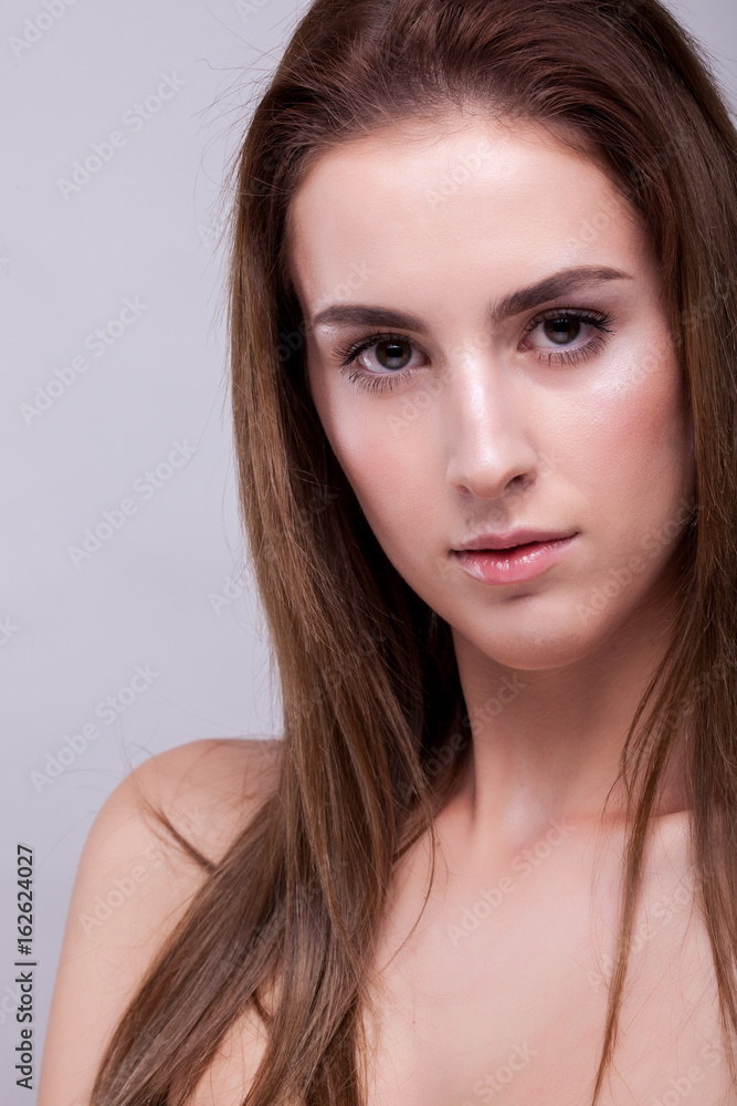 Portrait of attractive woman with perfect skin and natural makeup on gray background in studio photo. Beauty and fashion.