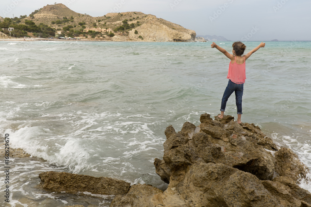 Girl with arms raised on the rocks