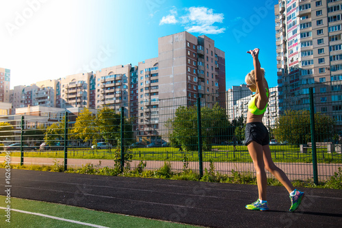 young fitness woman runner stretching hands before run on stadium in summer day
