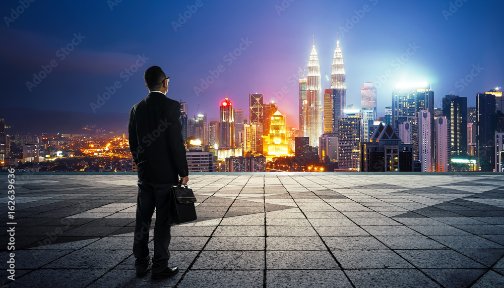 Businessman looking and thinking at roof top with modern city skyline background , night scene .