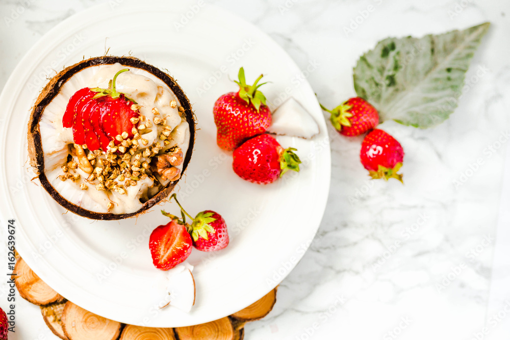 Ice cream with peanut butter, buckwheat and strawberries on coconut cup.Marble background.Vegan or diet food concept. Ice cream with peanut butter, buckwheat and strawberries on coconut cup.Marble background.Vegan or diet food concept.