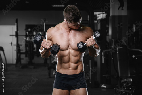 Muscular handsome athletic bodybuilder fitness model posing after exercises in gym on diet .