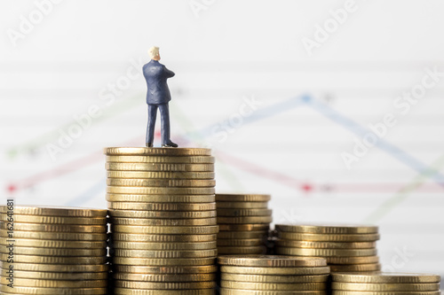 Miniature model of businessman thinking with project for investment standing coin.