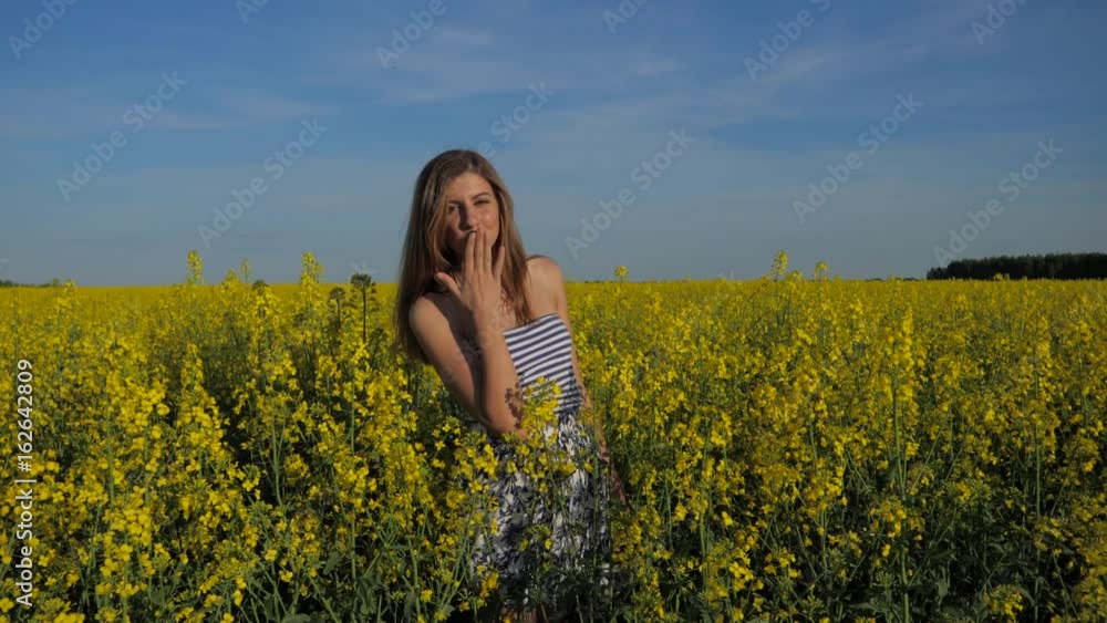 Smiling brunette girl standing in field of yellow flowers and sends a kiss. Smiling brunette girl standing in field of yellow flowers and sends a kiss.