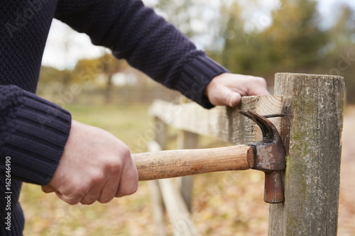Mature Man Removing Nail From Fence Being Repaired © Monkey Business