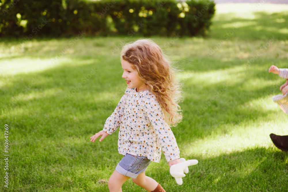 Cute little girl running and playing at park in warm sunny day. Strolling and holding rabbit toy in hands Cute little girl running and playing at park in warm sunny day. Strolling and holding rabbit toy in hands