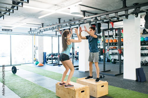 Young fit couple exercising in gym, doing box jumps.