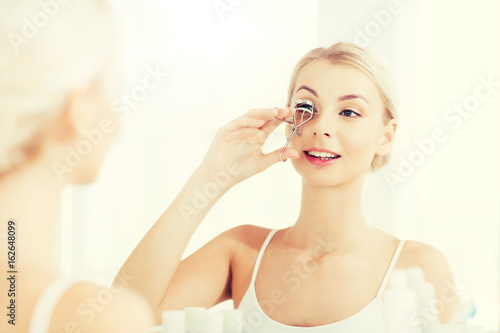 woman with curler curling eyelashes at bathroom