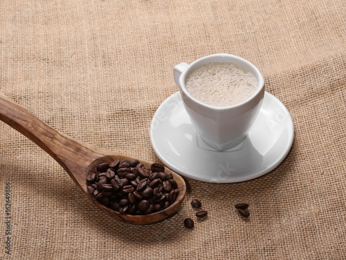 pile coffee beans, cup and wooden spoon on jute background, texture 