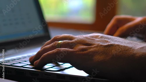 Man entering figures in speadsheet on laptop screen, indoors in low light, in front of window, close up panning up to monitor.
