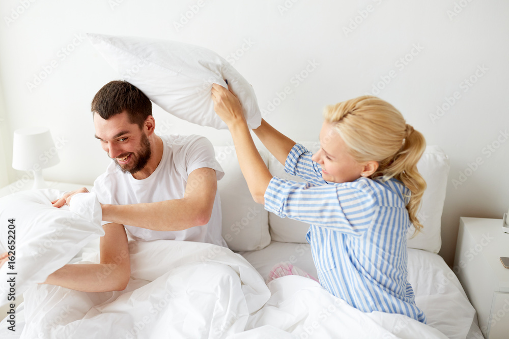 Fototapeta premium happy couple having pillow fight in bed at home