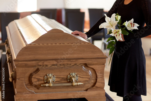 Obraz na plátně woman with lily flowers and coffin at funeral