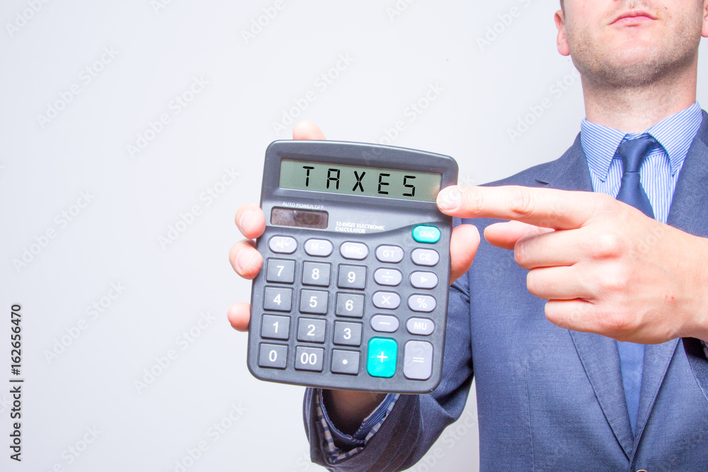 Young businessman pointing on calculator. Taxes business concept Calculator with TAXES on display Young businessman pointing on calculator. Taxes business concept Calculator with TAXES on display
