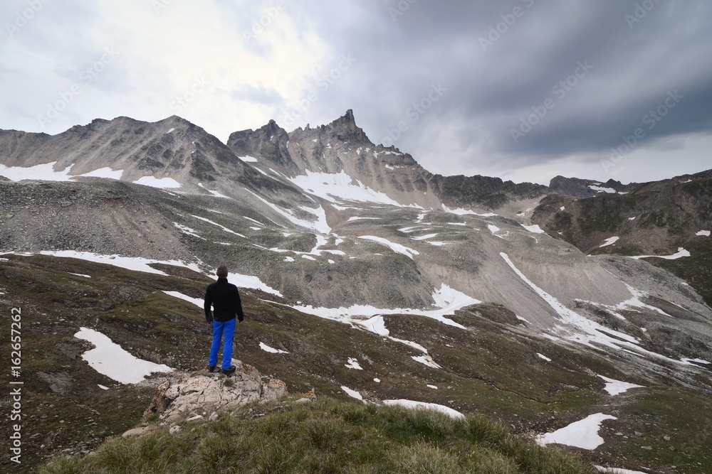 Hiker pauses to watch the mountain  aiguille du Dome ,Grande Sassiere valley, Tarentaise, Savoy, France