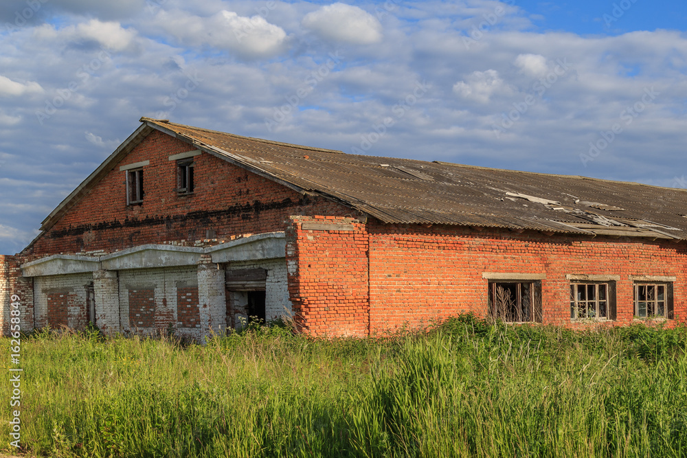 Abandoned building of red brick, overgrown with grass