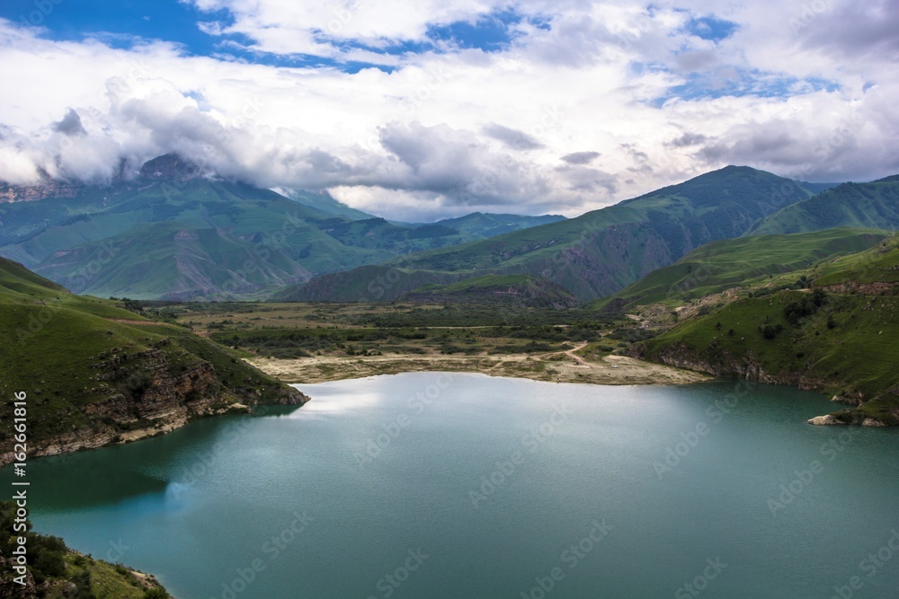 Горный пейзаж, красивый вид на живописное озеро в горном ущелье, облачная погода, зеленые склоны, дикая природа и горы Северного Кавказа