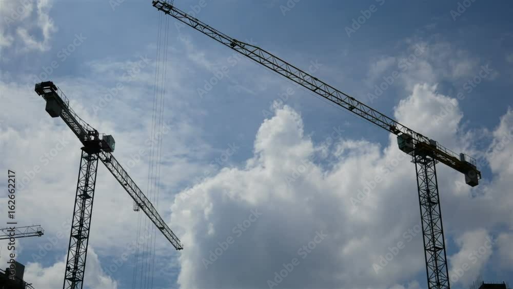 Construction cranes moving against the blue sky. The clouds are floating Construction cranes moving against the blue sky. The clouds are floating