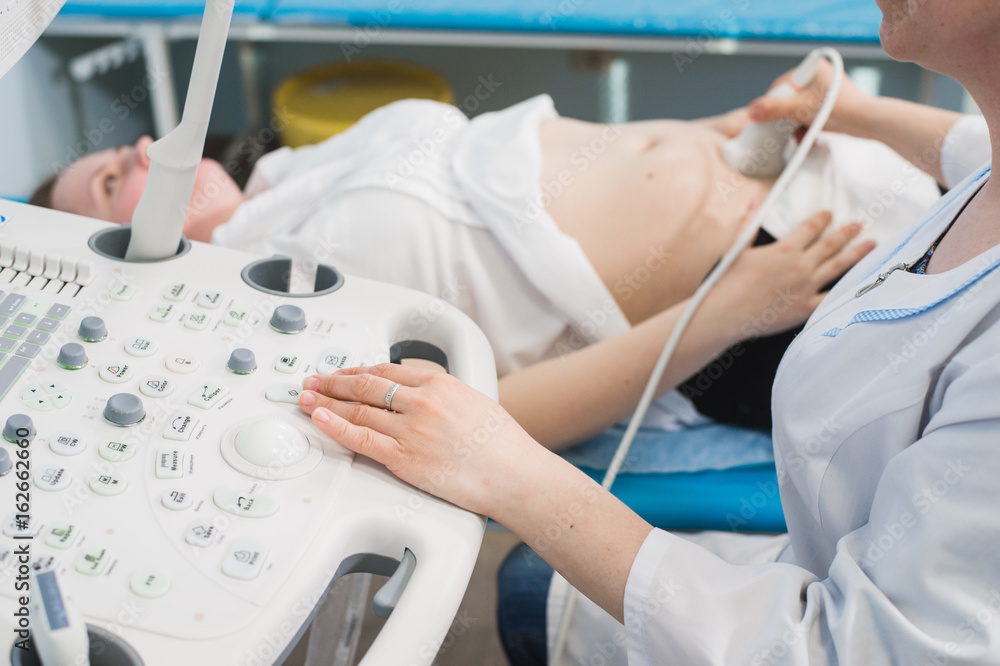 Close up of incognito doctor using ultrasound equipment for screening pregnant woman and press on buttons of special computer. Woman diagnosing in clinic Close up of incognito doctor using ultrasound equipment for screening pregnant woman and press on buttons of special computer. Woman diagnosing in clinic
