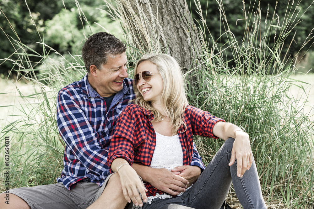 Fototapeta premium young laughing woman with his happy boyfriend sitting on the meadow