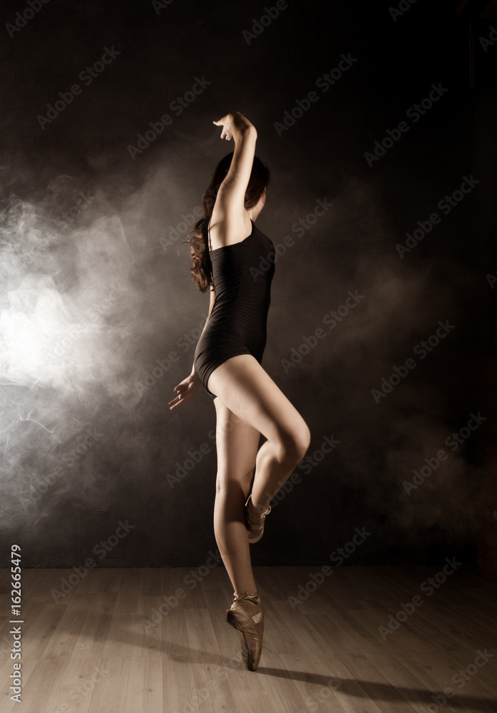 young beautiful ballet dancer in pointe shoes, dancing in a smoke on a dark background.