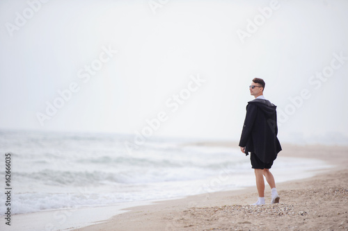 Young fashionable man walking along the beach