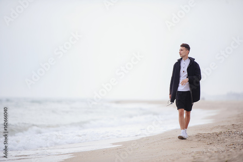 Young fashionable man walks along the beach, early morning time to think and postorit plans