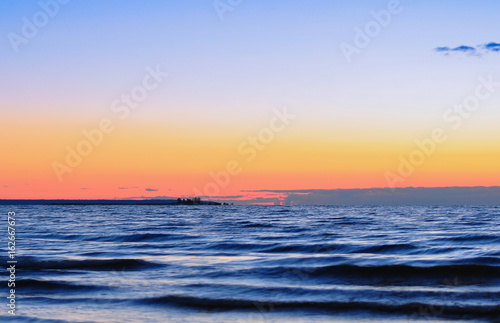 Dawn at the Ladoga. Waves and the small island on the lake in soft light of sunrise.