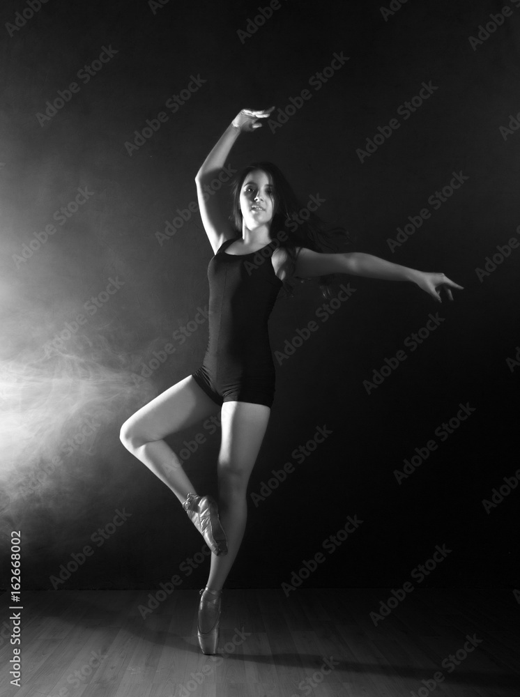young beautiful ballet dancer in pointe shoes, dancing in a smoke on a dark background. black and white