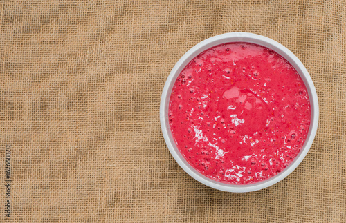 Bowl of fresh fruit sorbet smoothie made with frozen raspberries, bananas and apple juice on a sack cloth hessian background with copy space to left