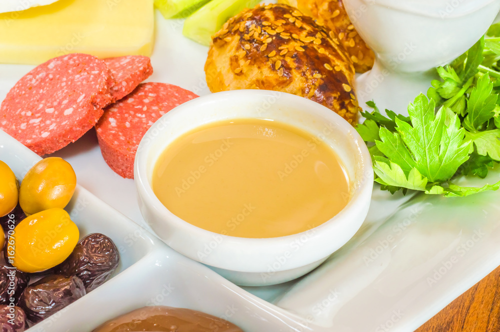 Closeup of traditional Turkish breakfast served in porcelain plate with olive, pastry, parsley, sausage, butter and sesame paste Closeup of traditional Turkish breakfast served in porcelain plate with olive, pastry, parsley, sausage, butter and sesame paste
