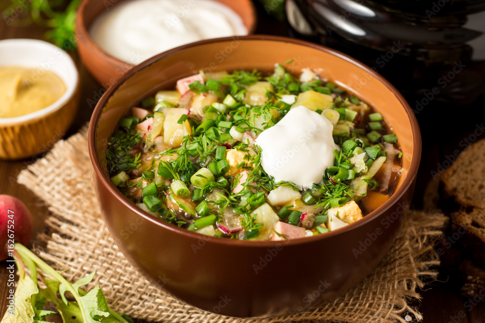 Okroshka. Traditional Russian summer cold soup with sausage, vegetables and kvass in bowl on wooden background.