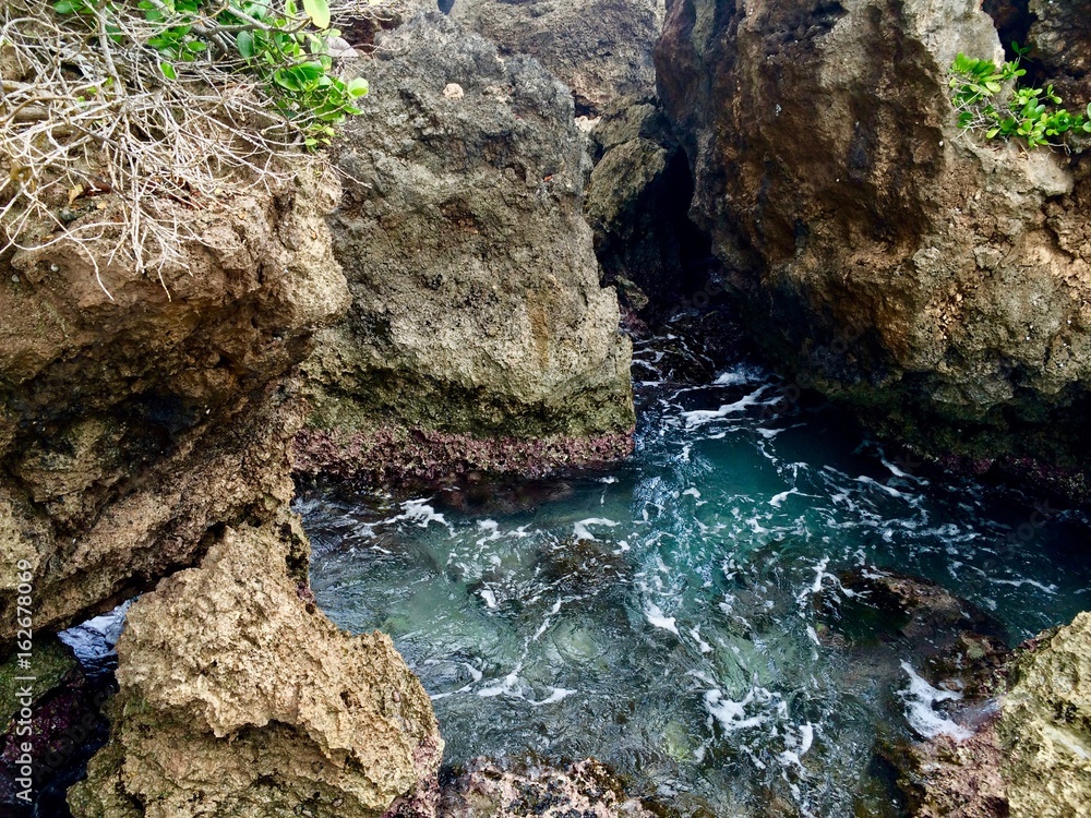 Secret cove: Stone rocks, cliff gorge, tropical lush greenery, & crystal clear turquoise water wave ocean in Boston Bay Jamaica in the Portland Parish (Caribbean island)