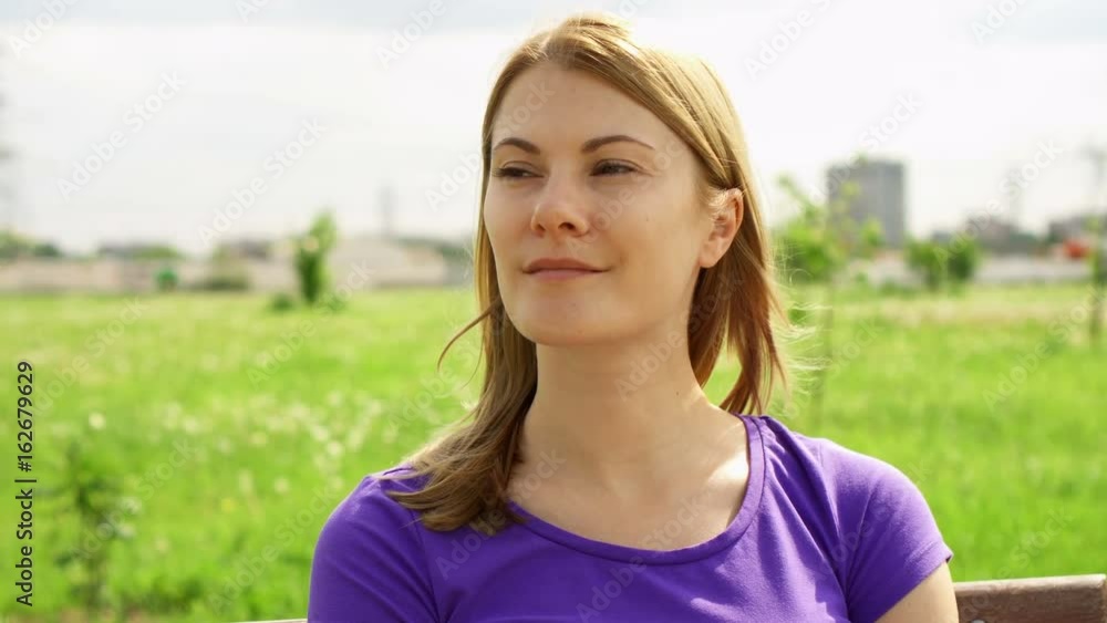 Slow Motion Happy Smiling Young Woman Enjoying Nature. Sitting on bench in green park. Freedom loneliness concept Slow Motion Happy Smiling Young Woman Enjoying Nature. Sitting on bench in green park. Freedom loneliness concept