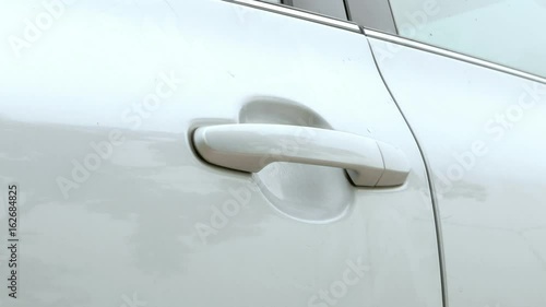 A man comes to the car and opening or closing car door in parking. The car color is blonde-gray. 