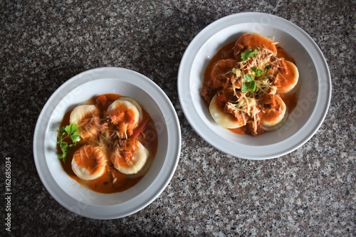 Upper view of two plates of sorrentinos - stuffed pasta - with sauce, parmesan cheese, and decorated with some parsley´s leaves