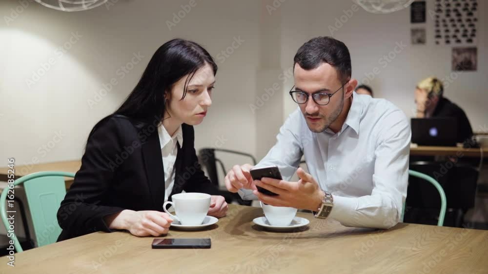 Business man and woman discussing something looking at the smartphone screen Business man and woman discussing something looking at the smartphone screen