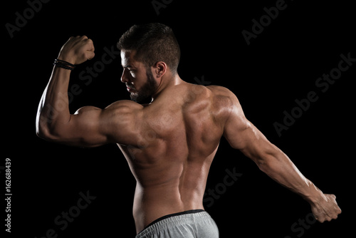 Muscular Man Flexing Muscles On Black Background © Jale Ibrak