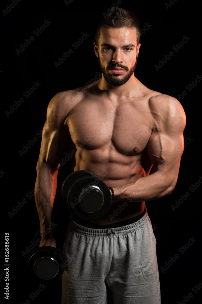 Model Exercising Biceps With Dumbbells On Black Background