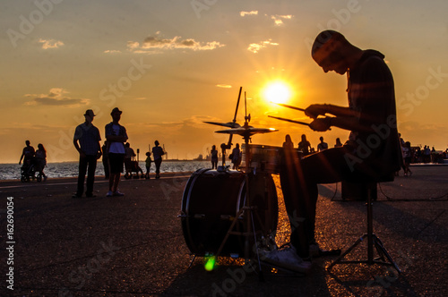 Silhouette of a street musician plays on drums near the sea
