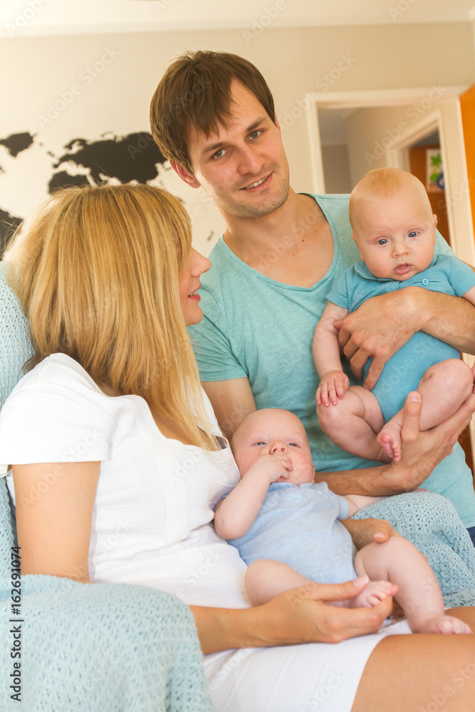 indoor portrait of young beautiful mother and father with baby, family with twins at home