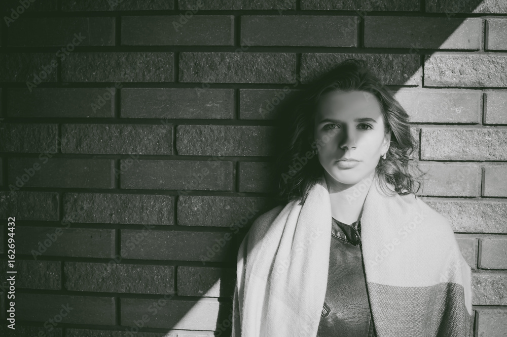 Portrait of young woman walking outdoors on warm autumn afternoon. Against a brick wall background Portrait of young woman walking outdoors on warm autumn afternoon. Against a brick wall background
