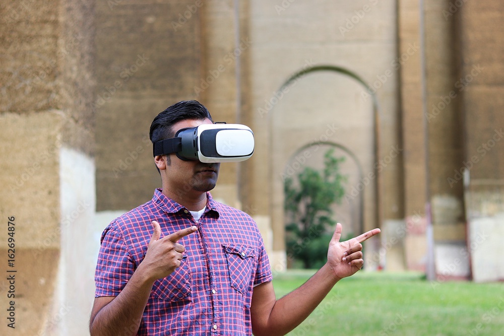 Young man wearing virtual reality goggles while standing under outdoor industrial archway tunnel