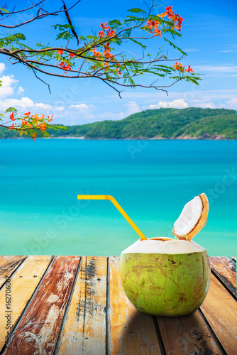 Coconut juice and straw on wood table in summer with blurred beach background , Summer holiday concept.