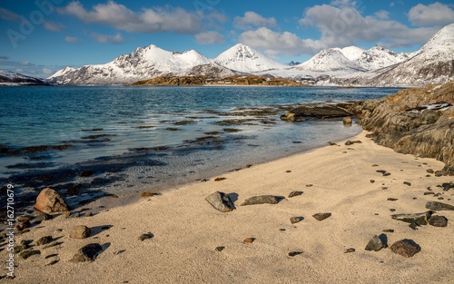 Blue sea, sand beach and snowy mountains during a sunny day. Tussoya, Kvaloya and Svinoya from Otervik ( Hillesoy), Troms, Norway photo