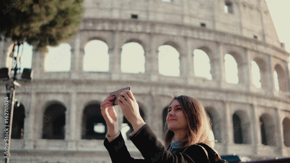 Young beautiful woman takes the selfie on smartphone. Woman walking in Rome, Italy near the Colosseum.