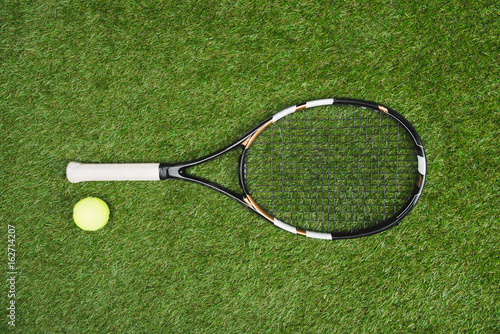 top view of tennis racket and ball lying on green lawn