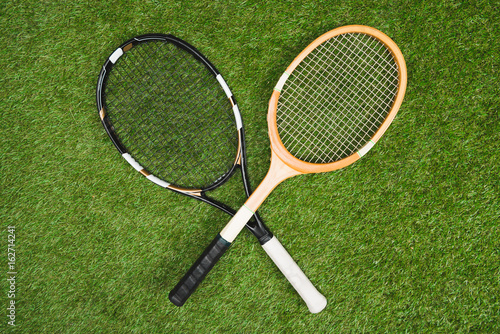 top view of plastic tennis and wooden badminton rackets on green lawn