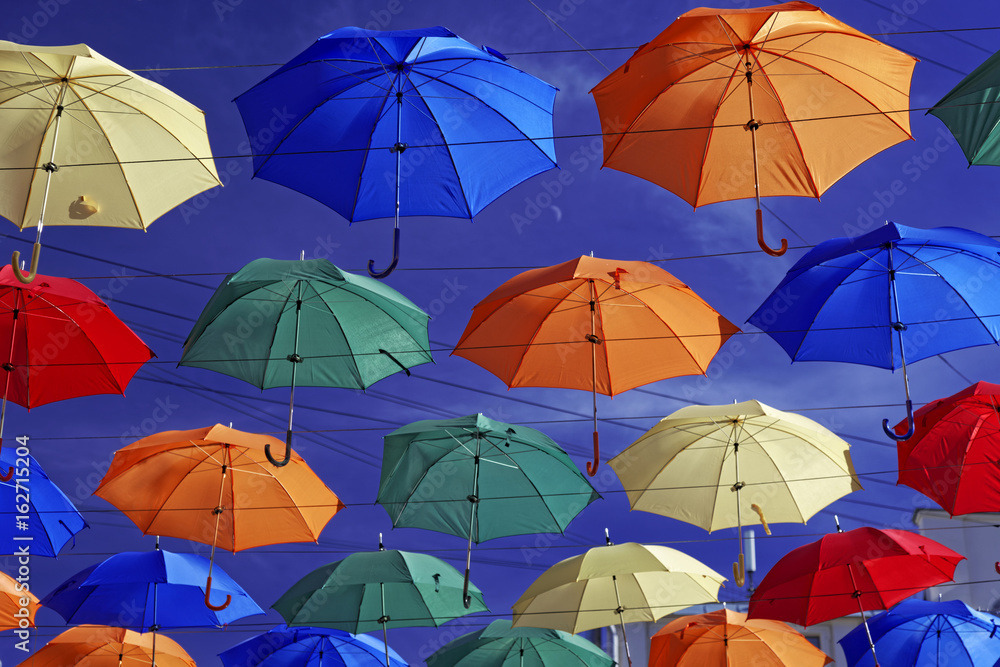 Multi-colored umbrellas in sky above the street. Alley floating umbrellas
