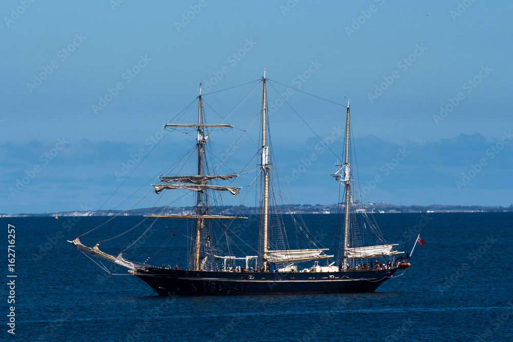 Schooner sailing ship boat moored in ocean bay against blue sky